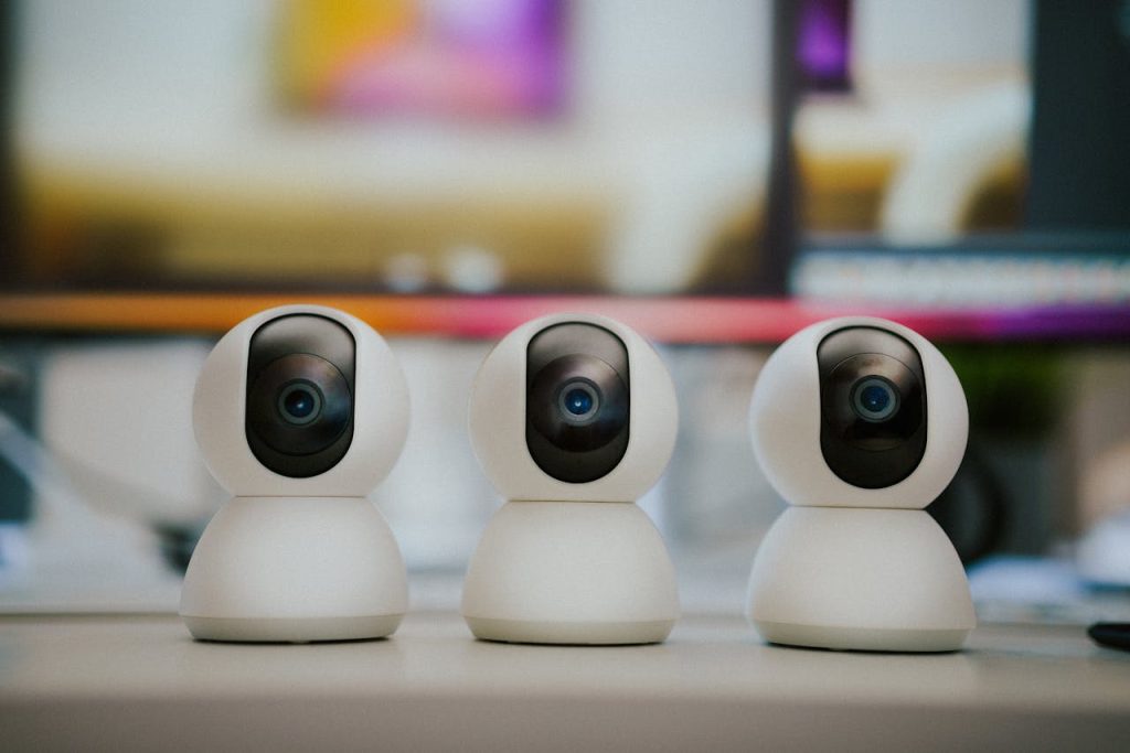 pexels-photo-28117882 Three modern smart home security cameras placed on a table indoors with a blurry background.